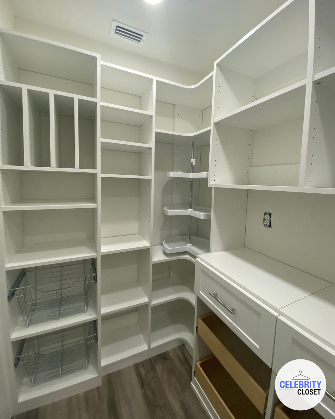 Empty white built-in closet with shelves, drawers, and wire baskets, with a wood floor and ceiling vent.