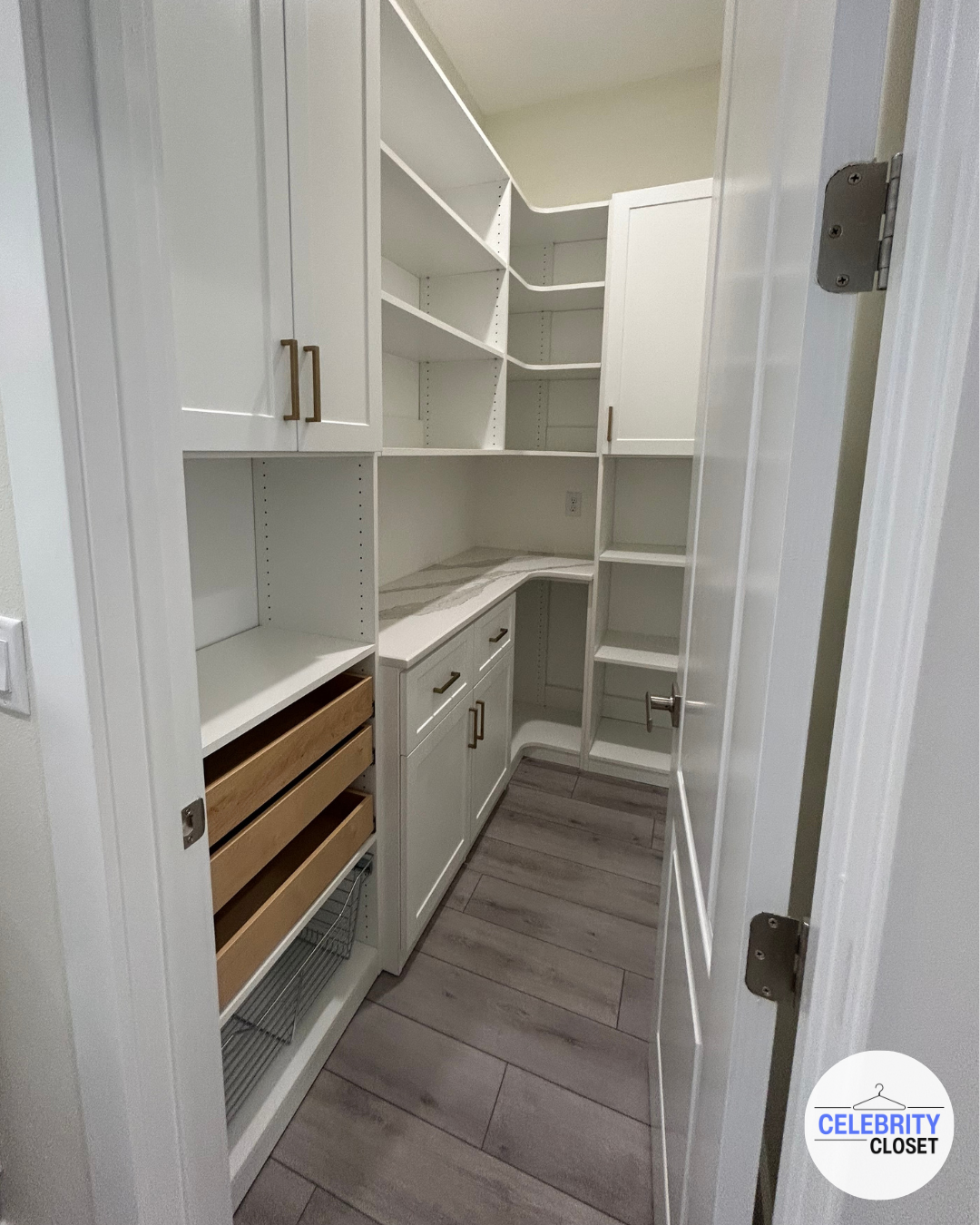 Empty white pantry closet with open door, multiple shelves, cabinets with handles, and wooden wine racks on the bottom left, with wood-look tile flooring.