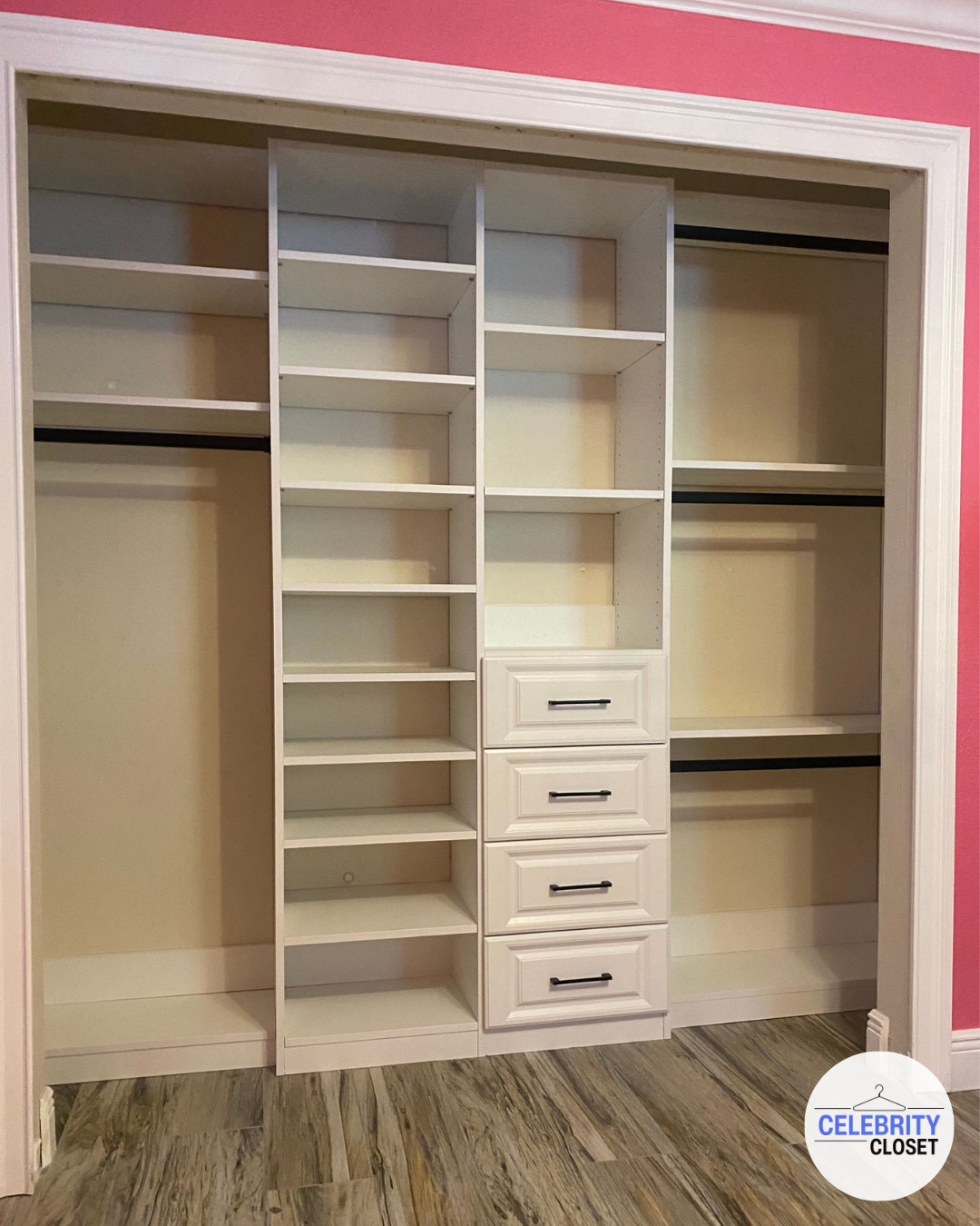 Empty white closet with shelves, drawers, and hanging rods, pink wall in background, wooden floor.