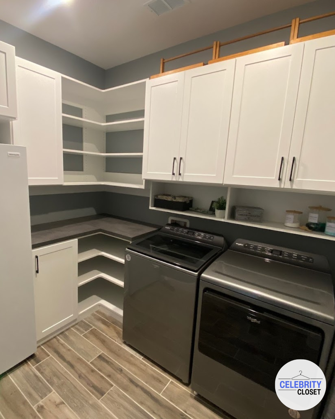 Laundry room with white cabinets, open shelving, and gray washing machine and dryer, wood-look flooring.