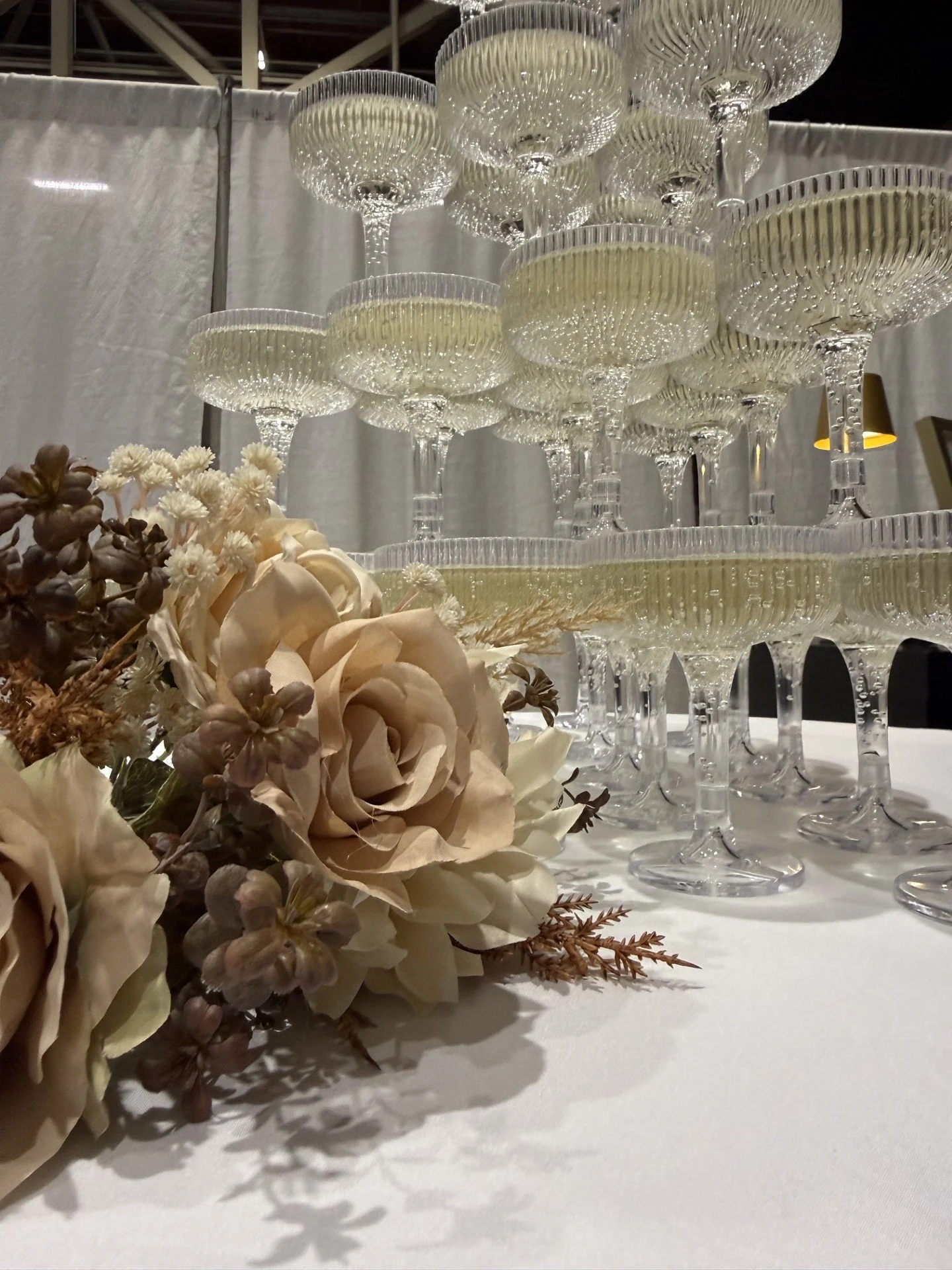 A floral centerpiece with cream-colored flowers and a tiered display of empty glass dessert cups on a white tablecloth.