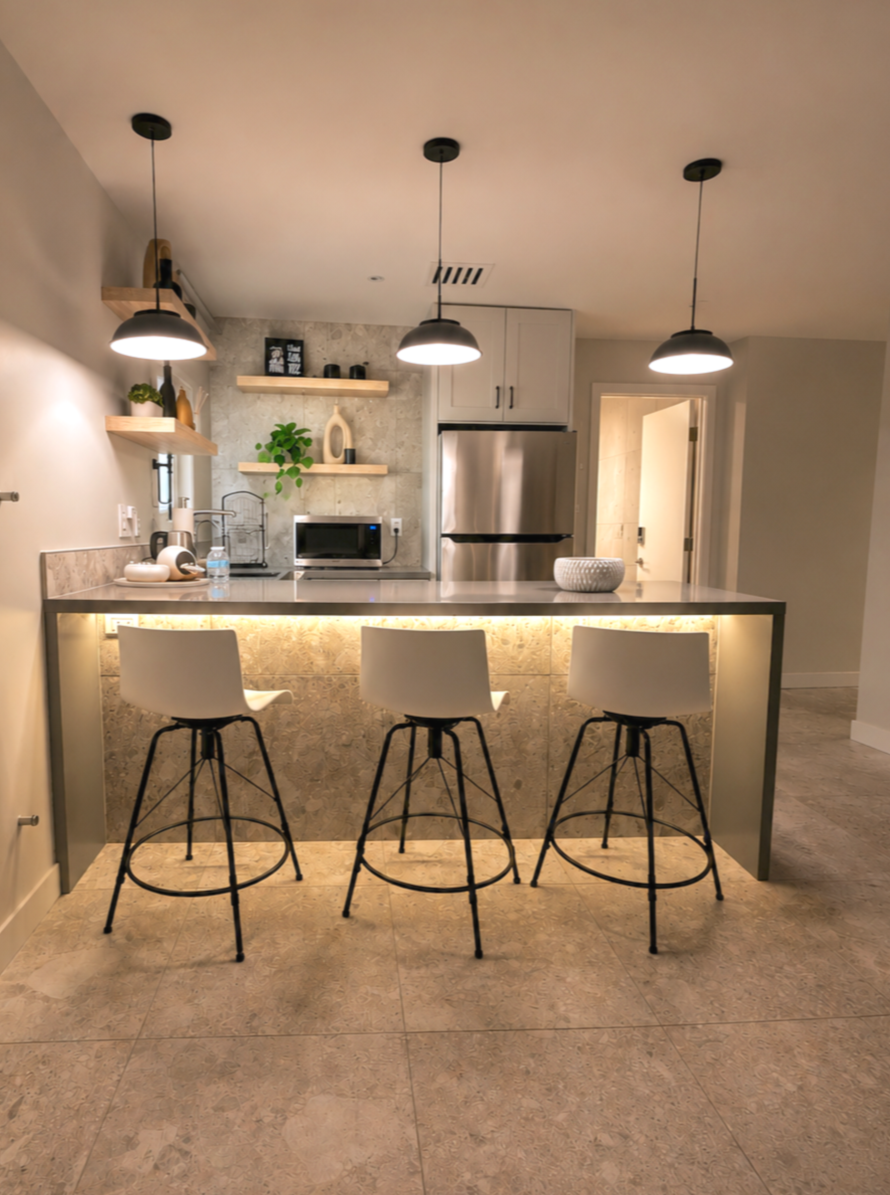 Modern kitchen and breakfast bar area at Green Orange Studio with pendant lighting, white stools, open shelving, and warm studio styling.