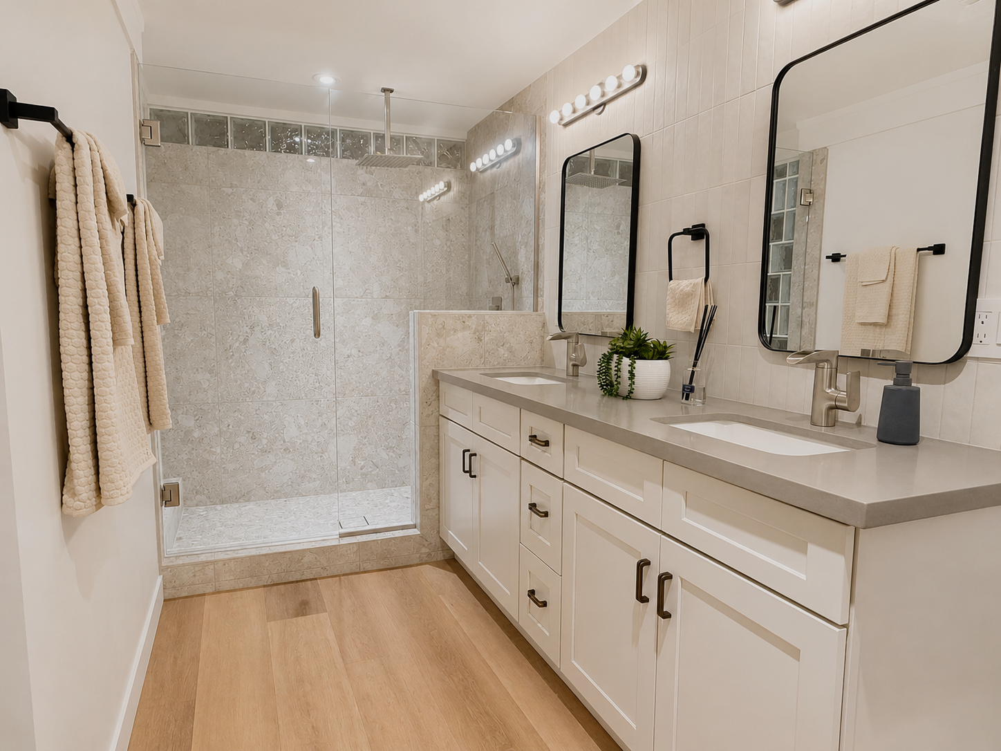 Bathroom with a double vanity, two mirrors, a plant, and a walk-in shower with glass doors and beige tiles.