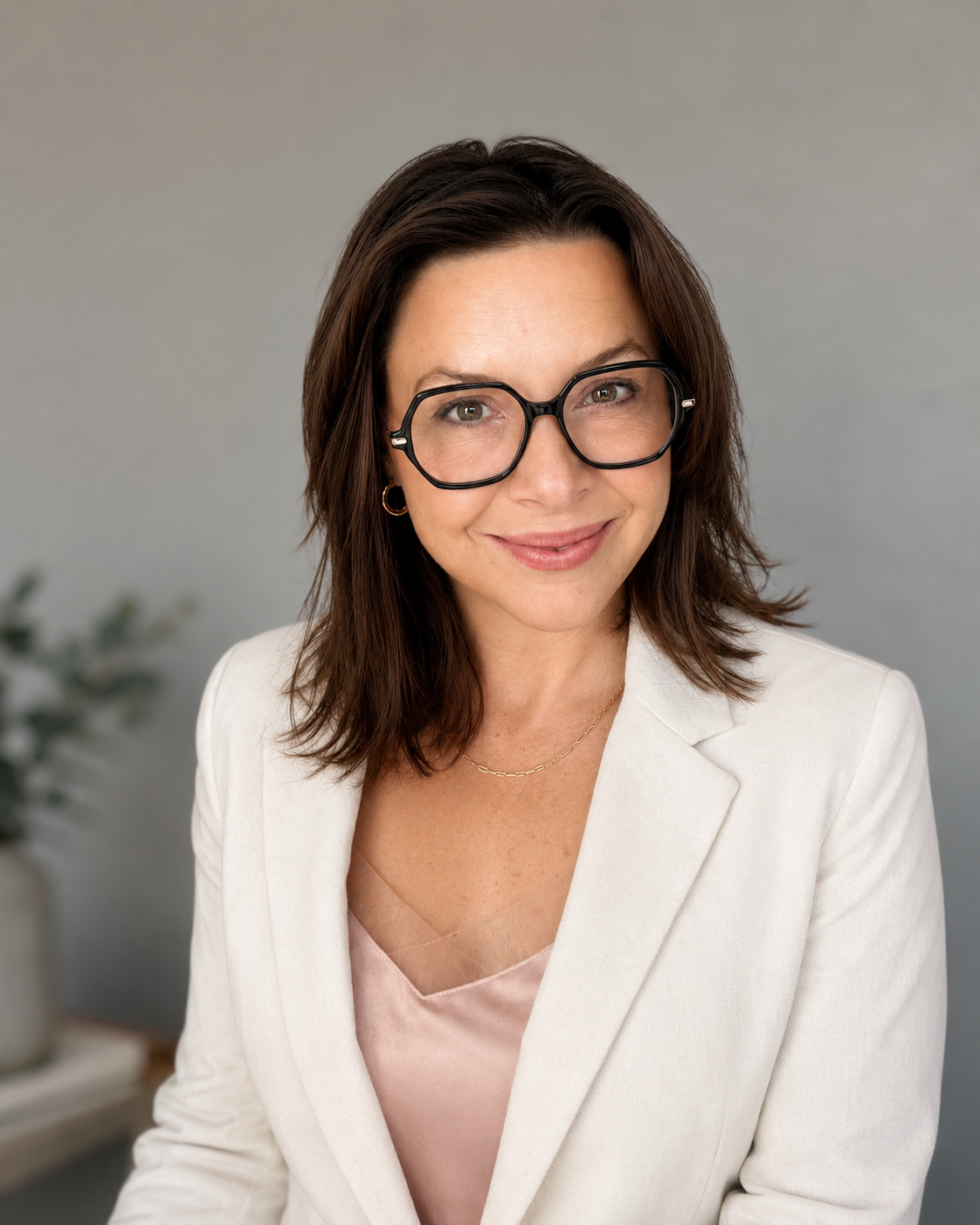 Professional portrait of leadership coach Gina in a white blazer and soft neutral top, smiling warmly against a clean grey background. Executive coaching, leadership development, emotional intelligence, confidence, and human-centered leadership
