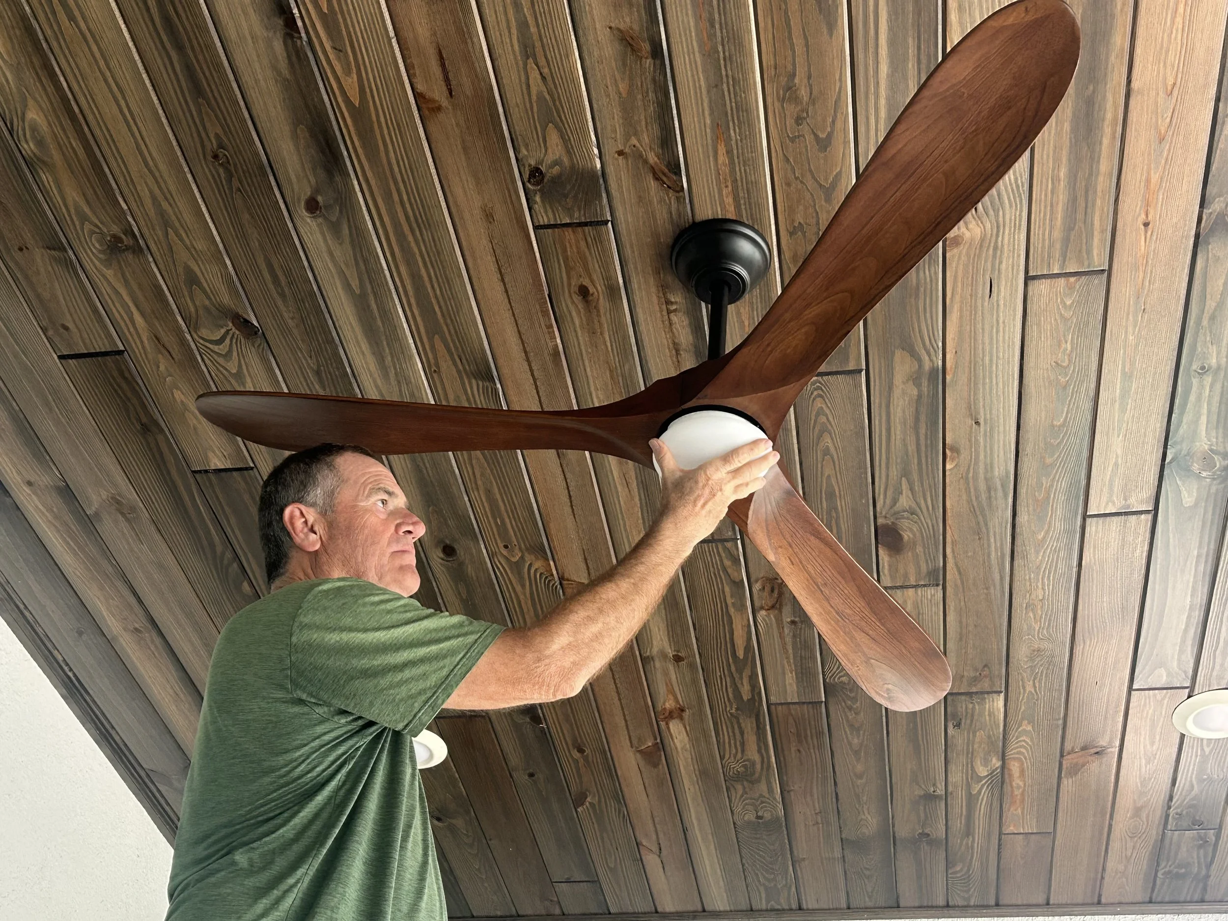 A man installing a ceiling fan on a wooden ceiling.