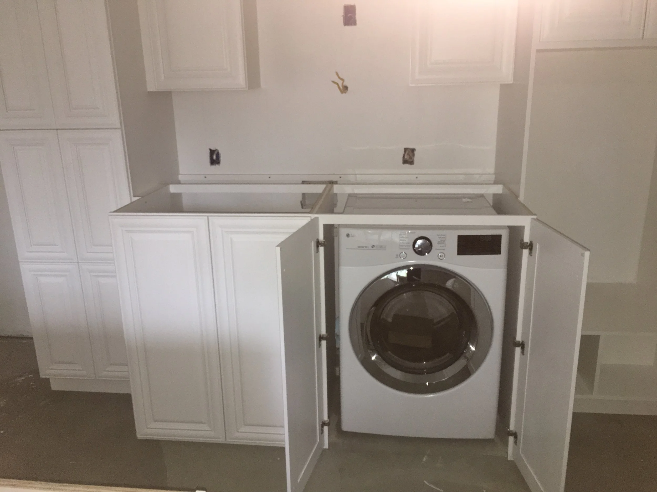 A laundry room with white cabinets and a front-loading washing machine and dryer stacked together. The cabinets have raised panel doors.