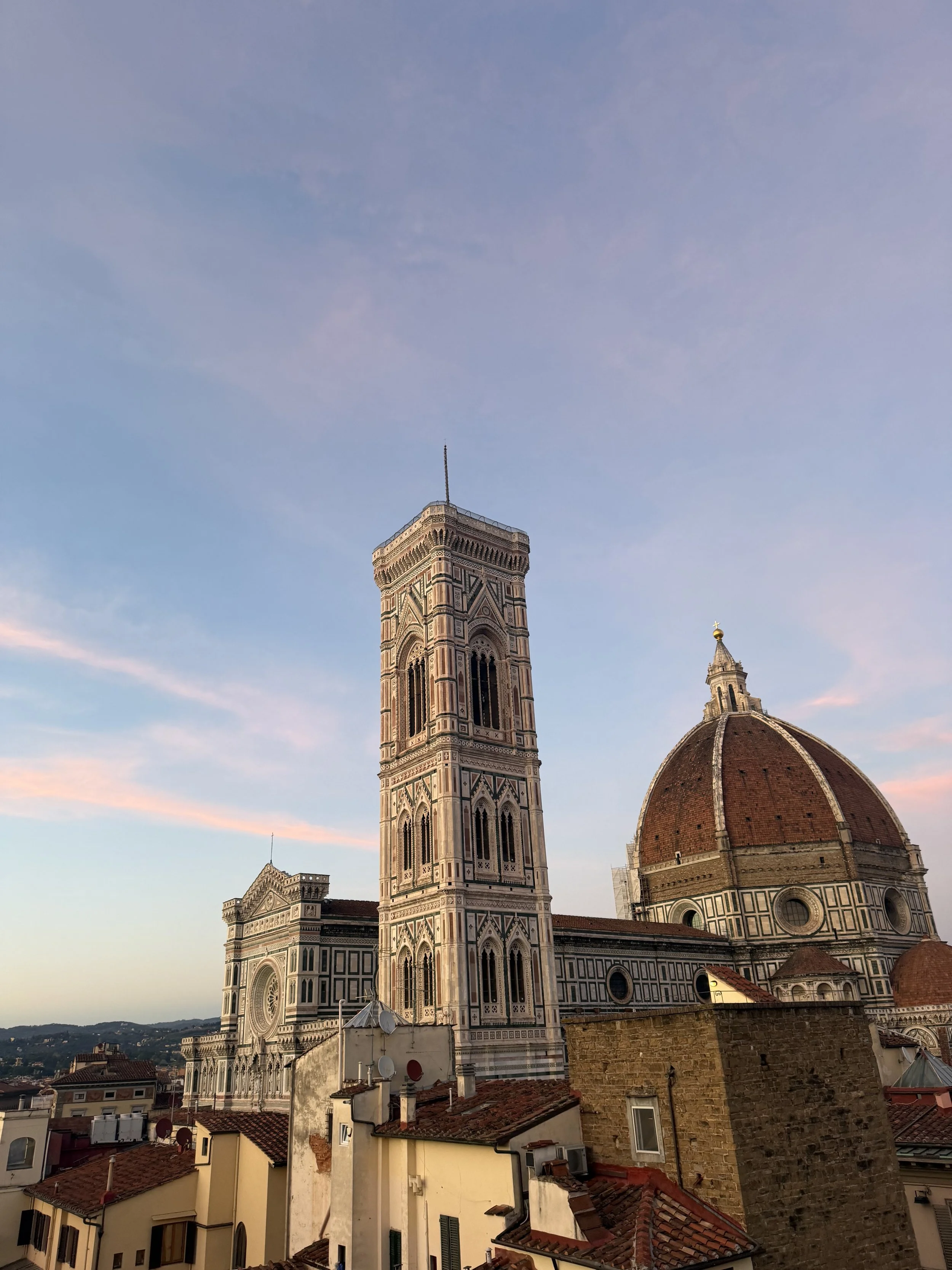The Florence Cathedral, also known as the Cathedral of Santa Maria del Fiore, with its distinctive marble exterior and the adjacent bell tower, under a partly cloudy sky during sunset in Florence, Italy.