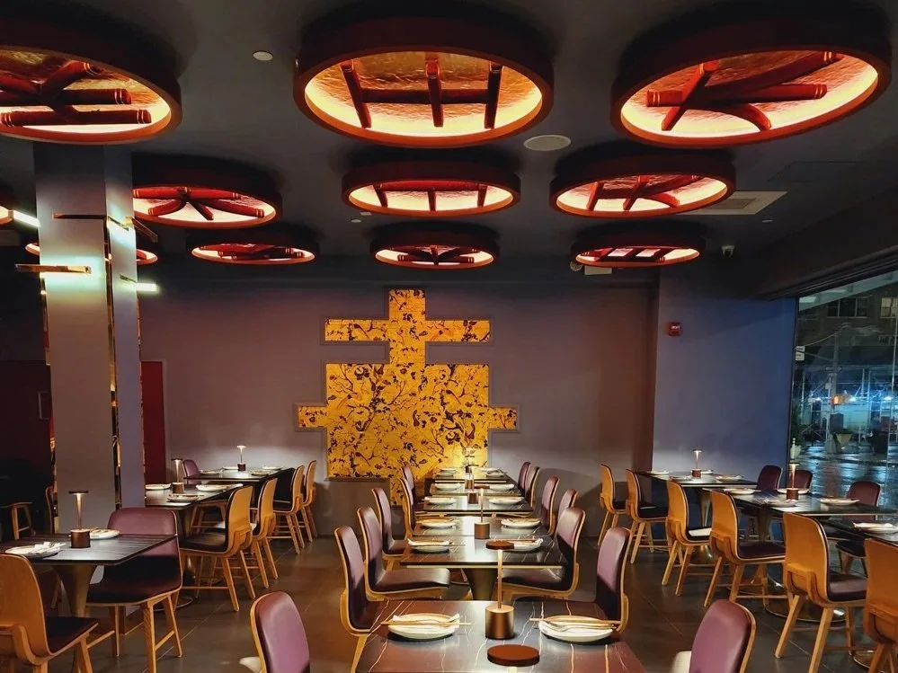 Empty restaurant with modern decor, circular ceiling lights, a large abstract yellow and black wall art, and tables set for dining.