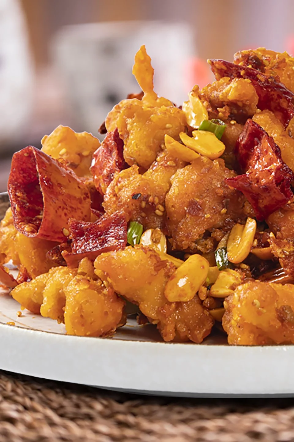 Close-up of a dish of fried chicken with peanuts, green onions, and red peppers on a plate.