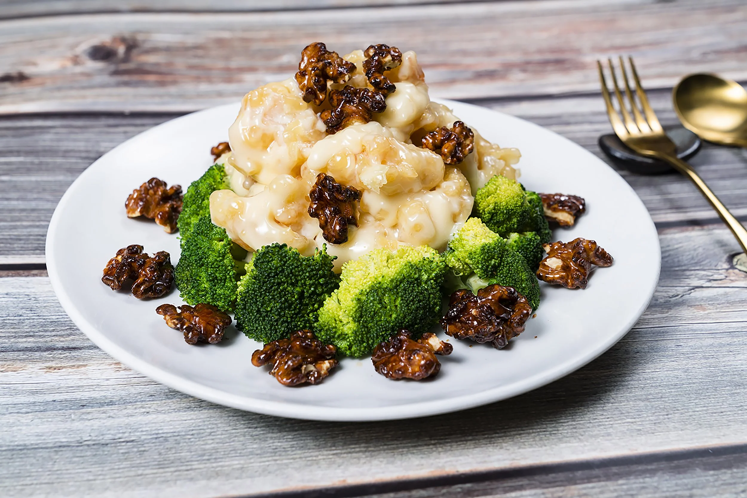 A plate of creamy cauliflower topped with walnuts and surrounded by broccoli florets on a rustic wooden table.