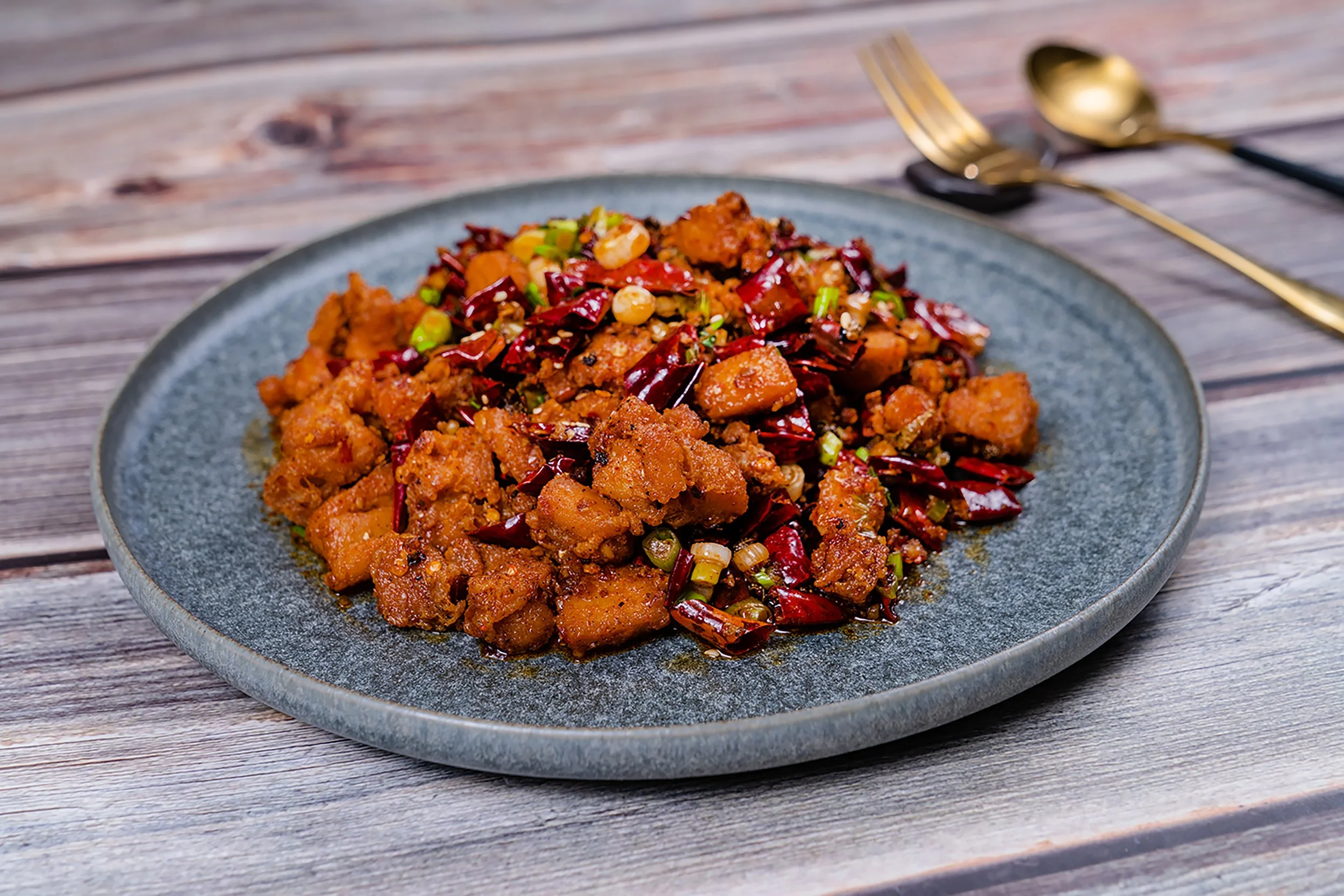 A plate of spicy stir-fried tofu with chili peppers and chopped green onions on a wooden table.