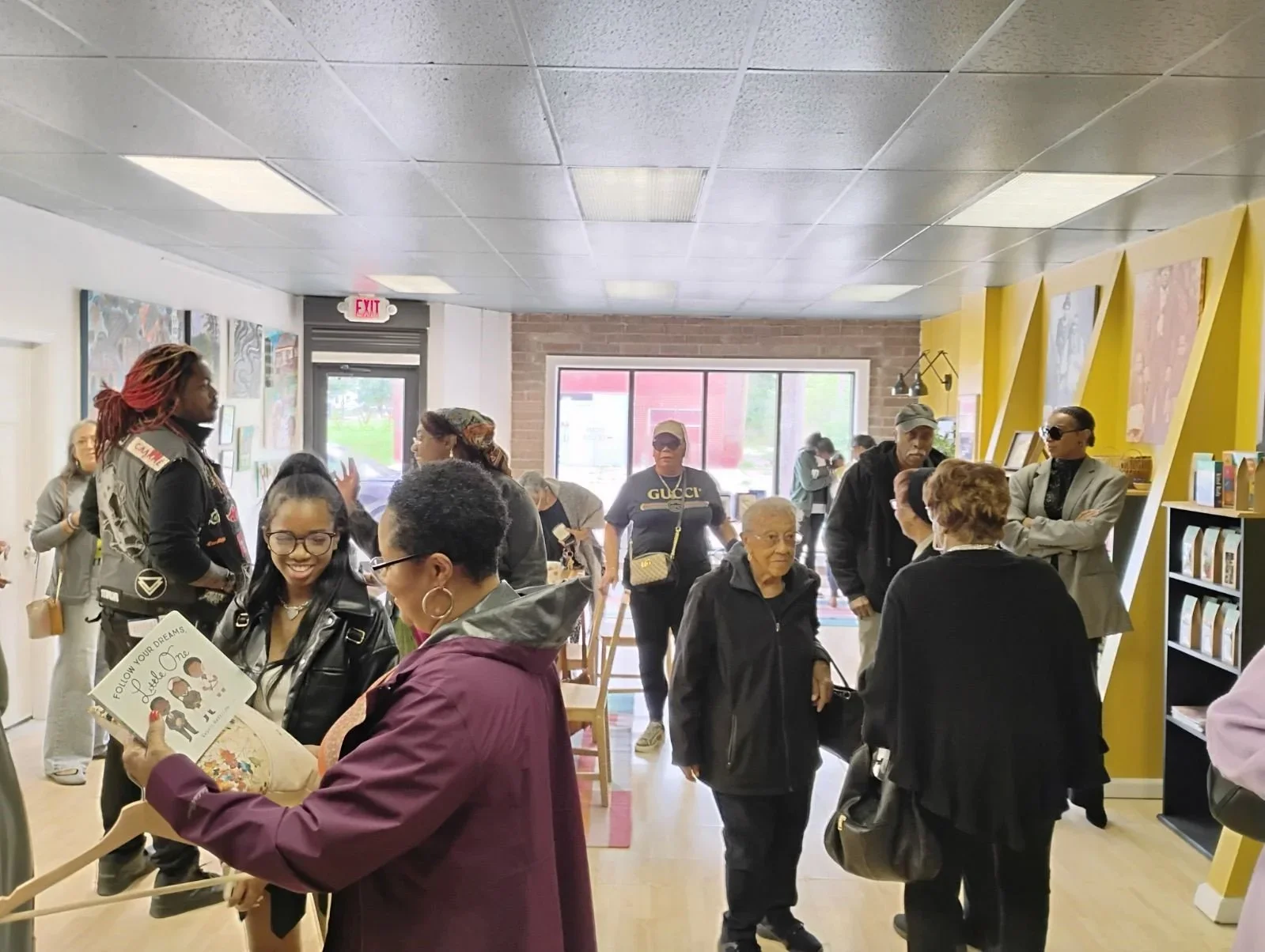 A group of diverse people socializing inside a bookstore or community center, with some looking at books and others chatting.