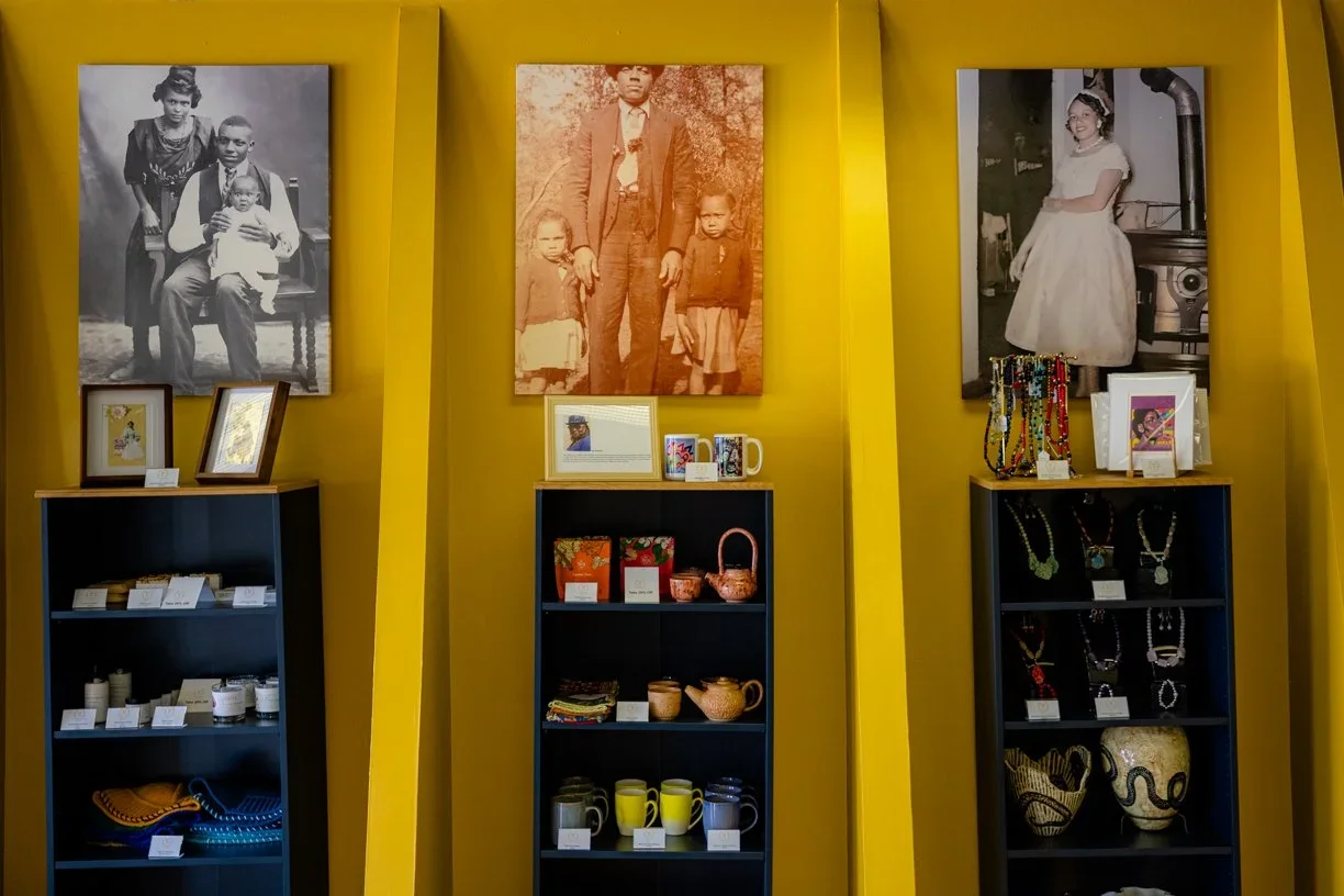 Display of framed family photos and jewelry, pottery, and souvenirs on black shelves against yellow walls.