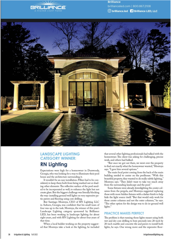 Exterior view of a house illuminated with landscape lighting at dusk, with a water feature in front and trees silhouetted in the background.