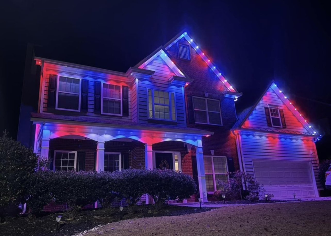 A two-story house decorated with red, white, and blue string lights for a festive occasion at night.