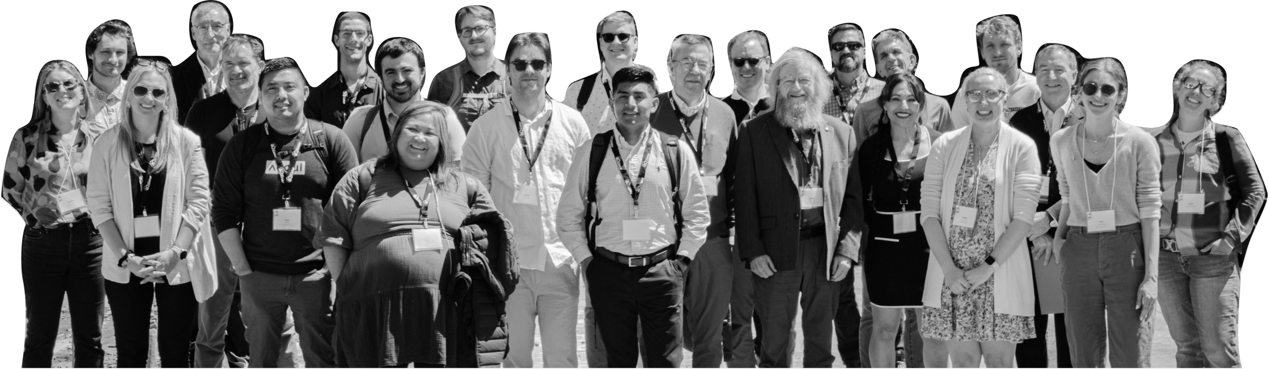 A group of around 20 people posing outdoors, smiling, with some wearing conference badges.