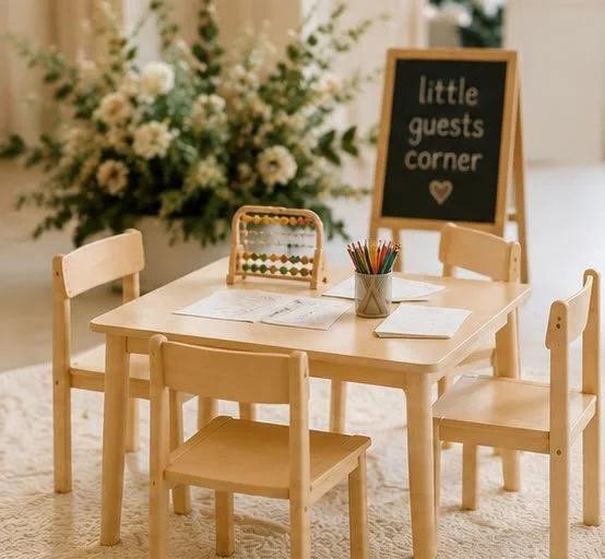 A small children's table with four chairs, a blackboard sign that says "little guests corner" with a heart, and a flower arrangement in the background.