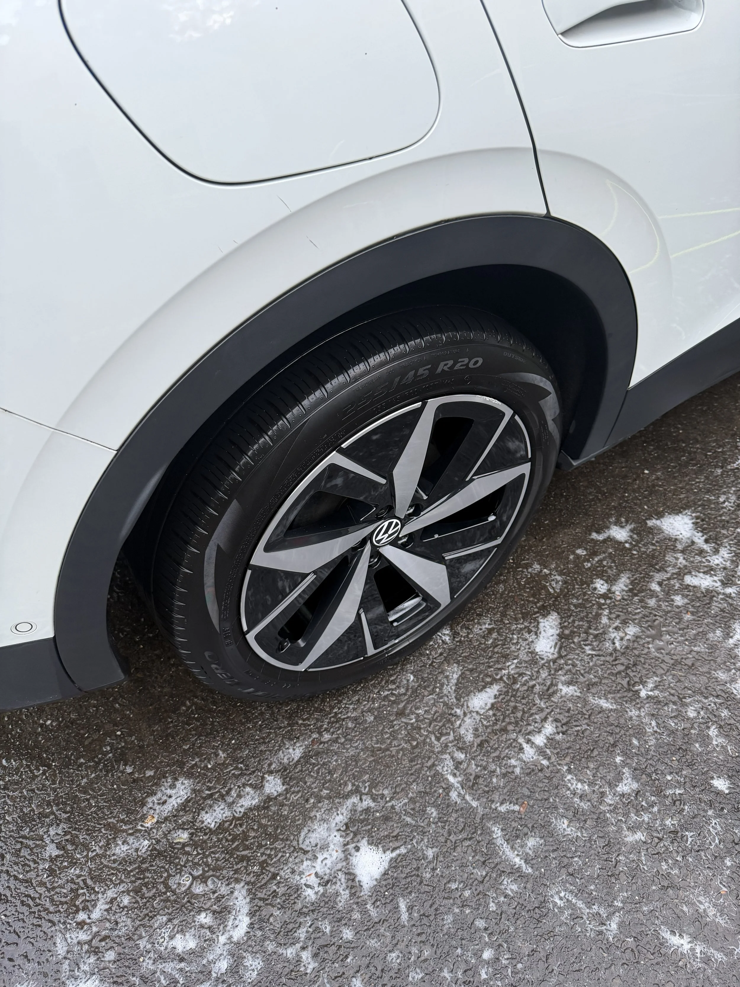 Close-up of a white Volkswagen vehicle's rear wheel and tire on a snowy, icy ground.