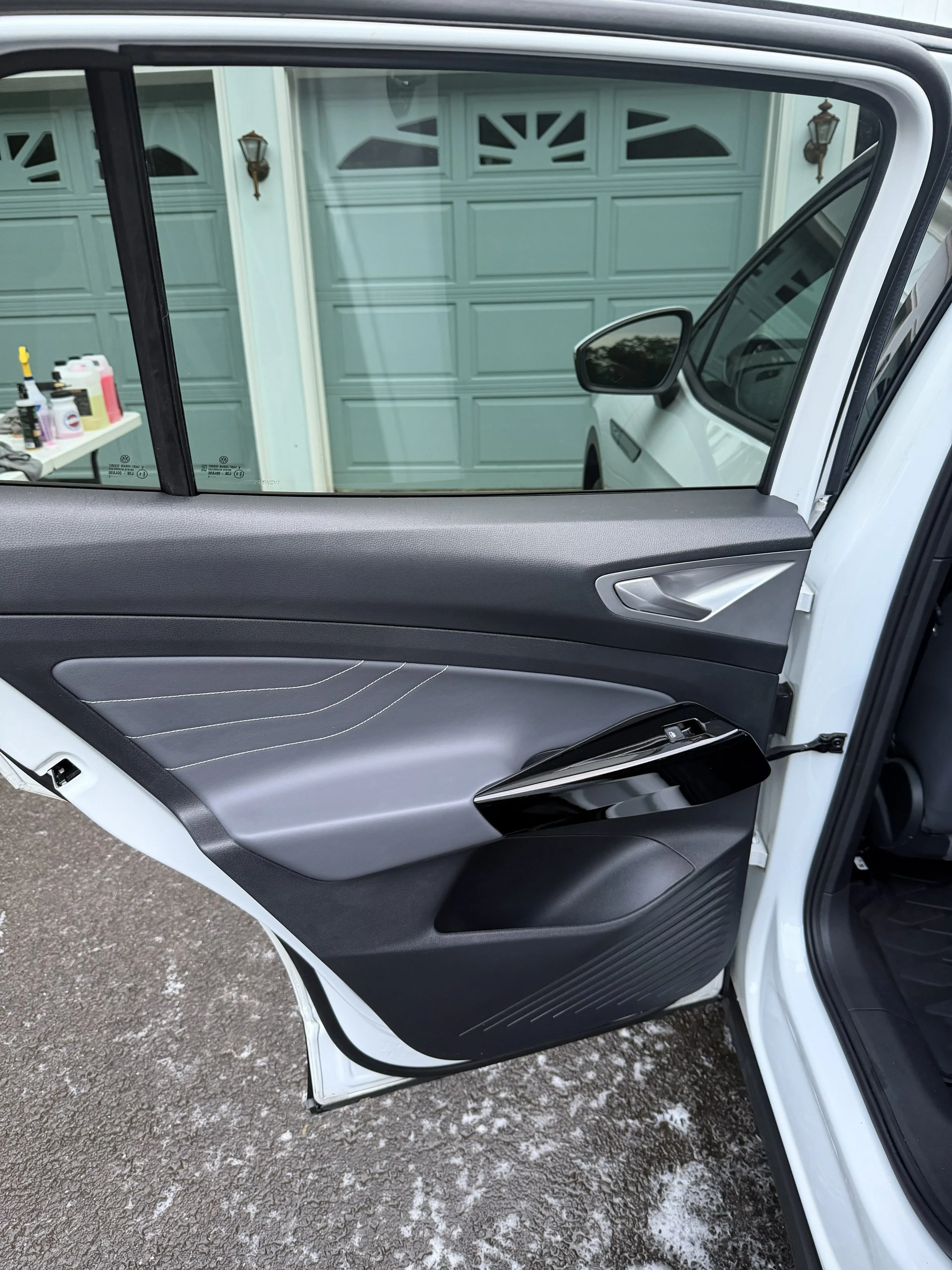 Open car door showing the interior door panel and side mirror, with a garage and some cleaning supplies visible through the window.