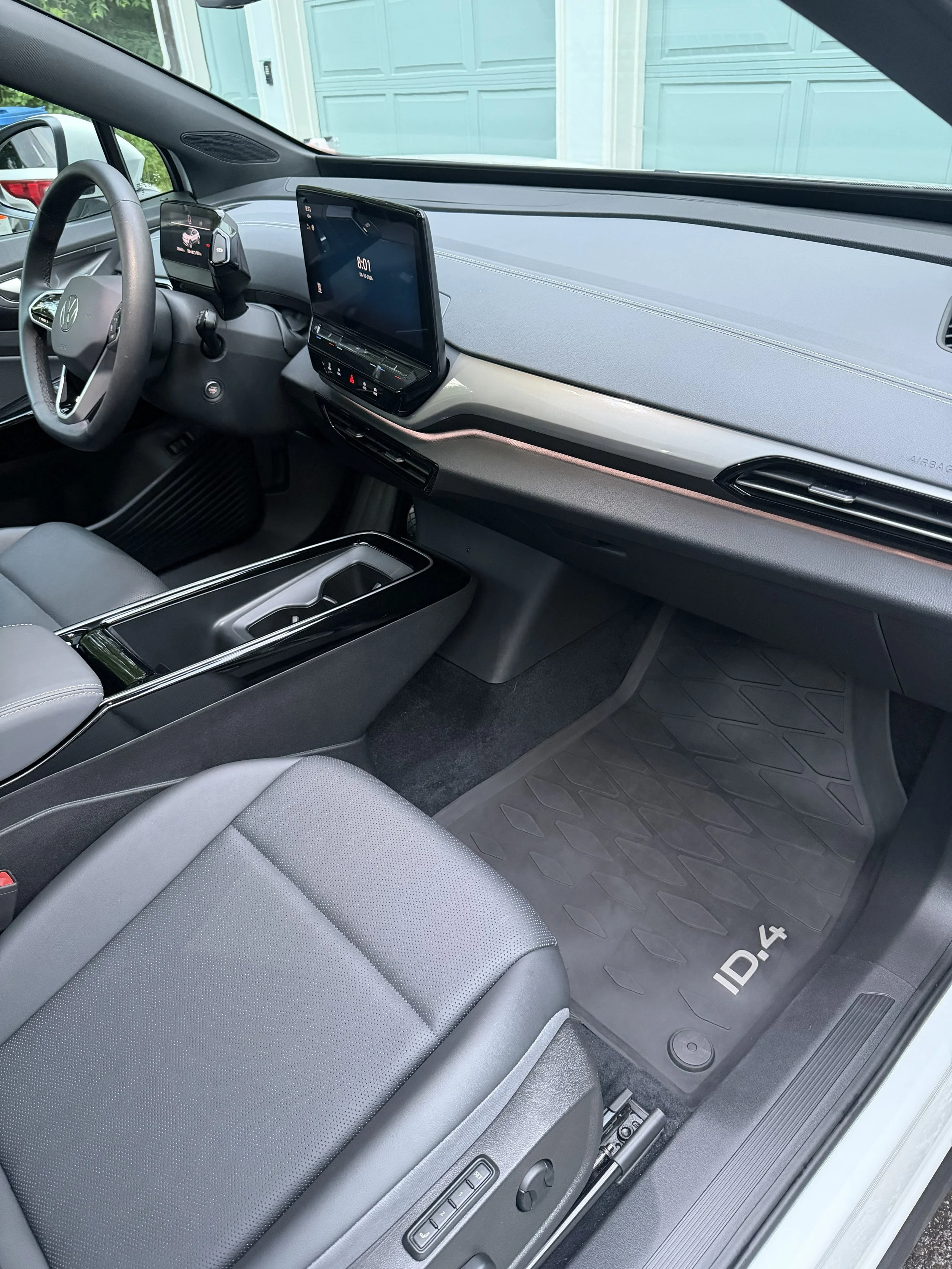 The interior of a modern Volkswagen ID.4 electric vehicle showing the driver's seat, digital dashboard, large central touchscreen, and floor mat.