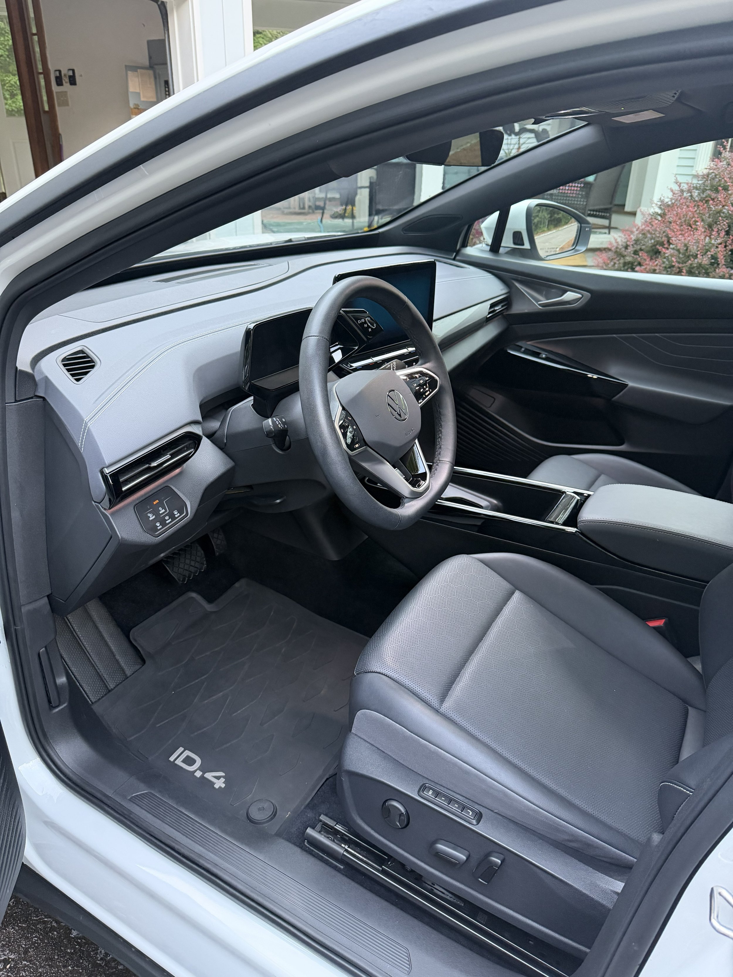 Interior of a white Volkswagen ID.4 electric car showing the steering wheel, dashboard, and front passenger seat with a black floor mat labeled ID.4.