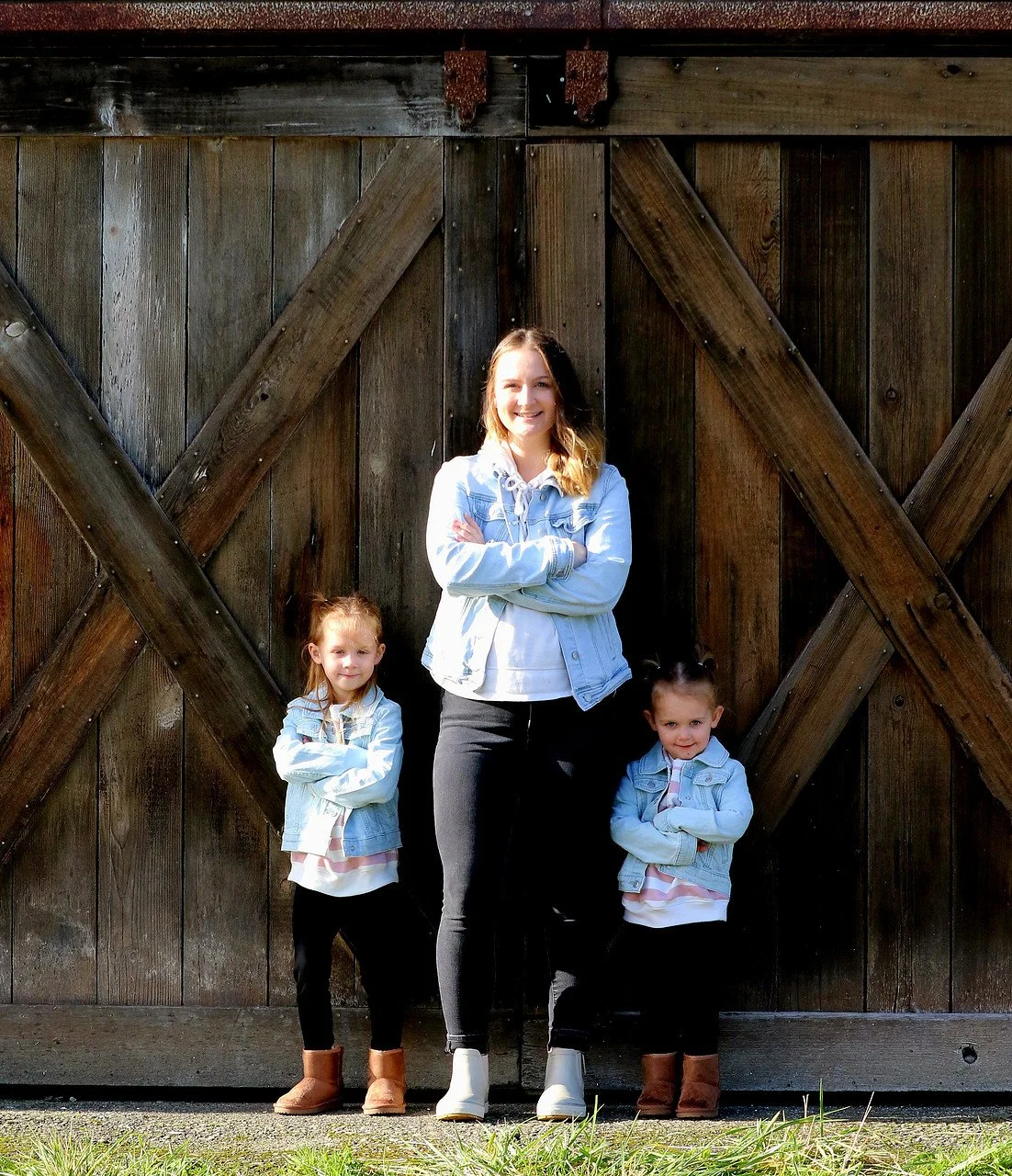 A woman and two young girls standing in front of a large wooden barn door with crossed beams.