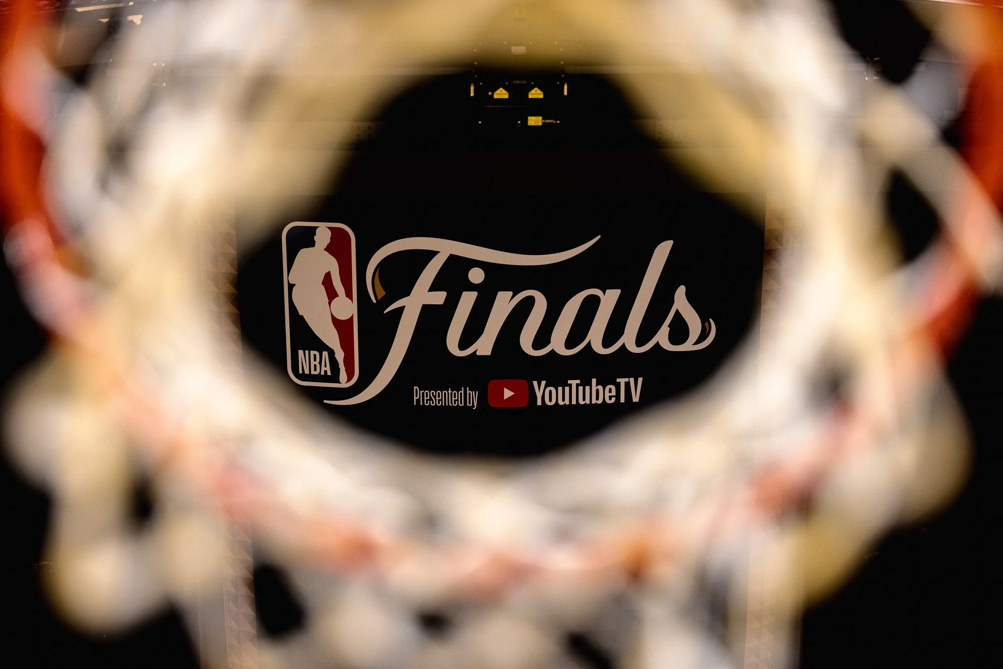 A basketball with NBA Finals logo and YouTube TV sponsorship seen through a tunnel of baseball bats.