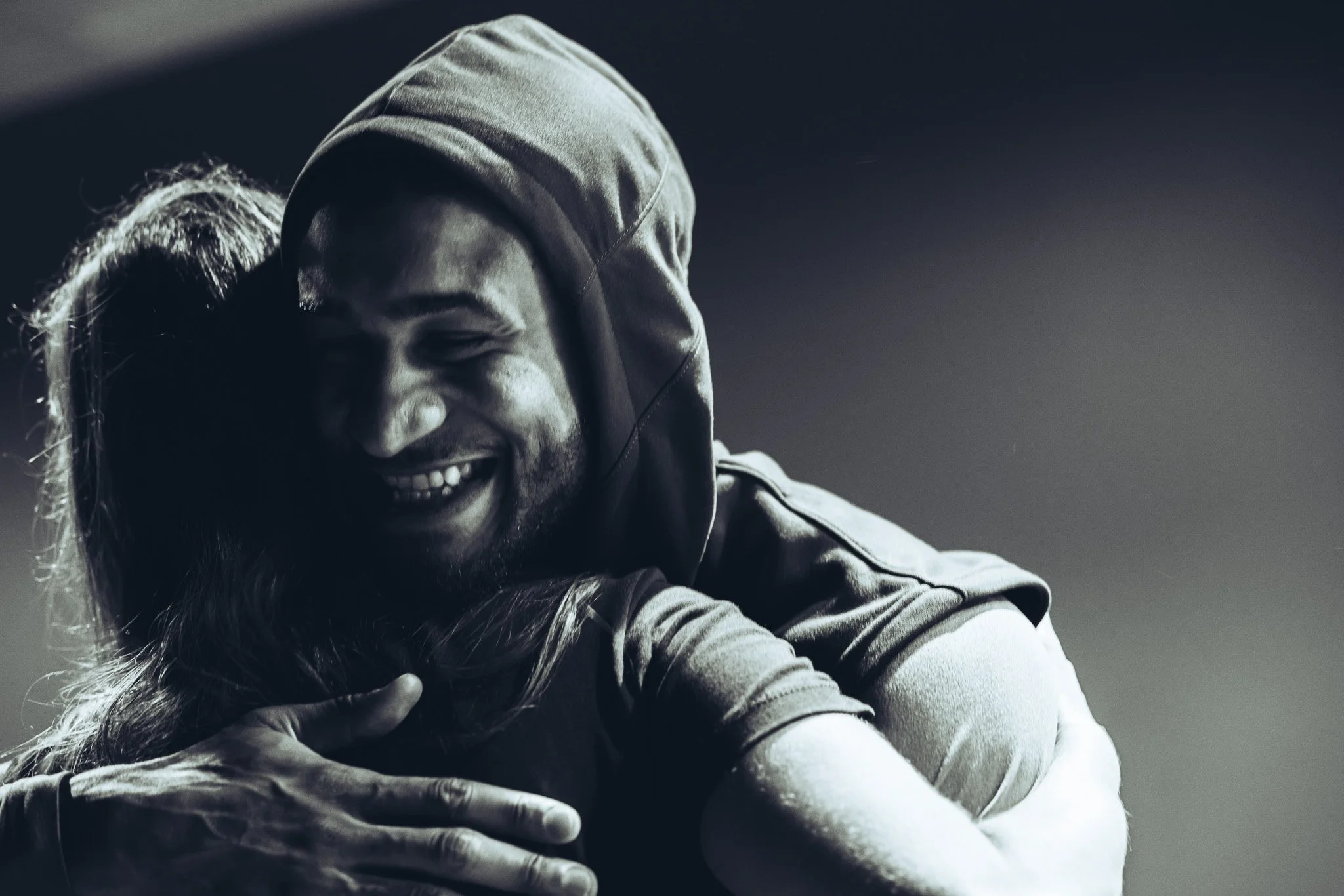 A man and woman embracing warmly, both smiling with eyes closed, in a black and white photo.