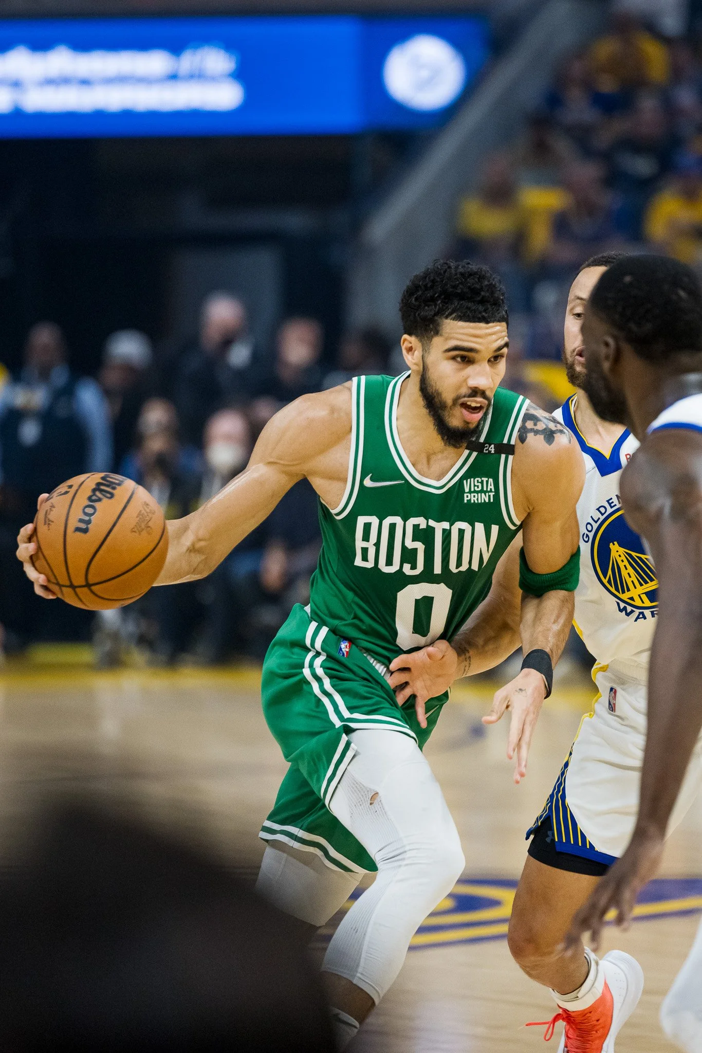 A basketball player from the Boston Celtics in green uniform dribbling the ball while being guarded by opponents during a game.