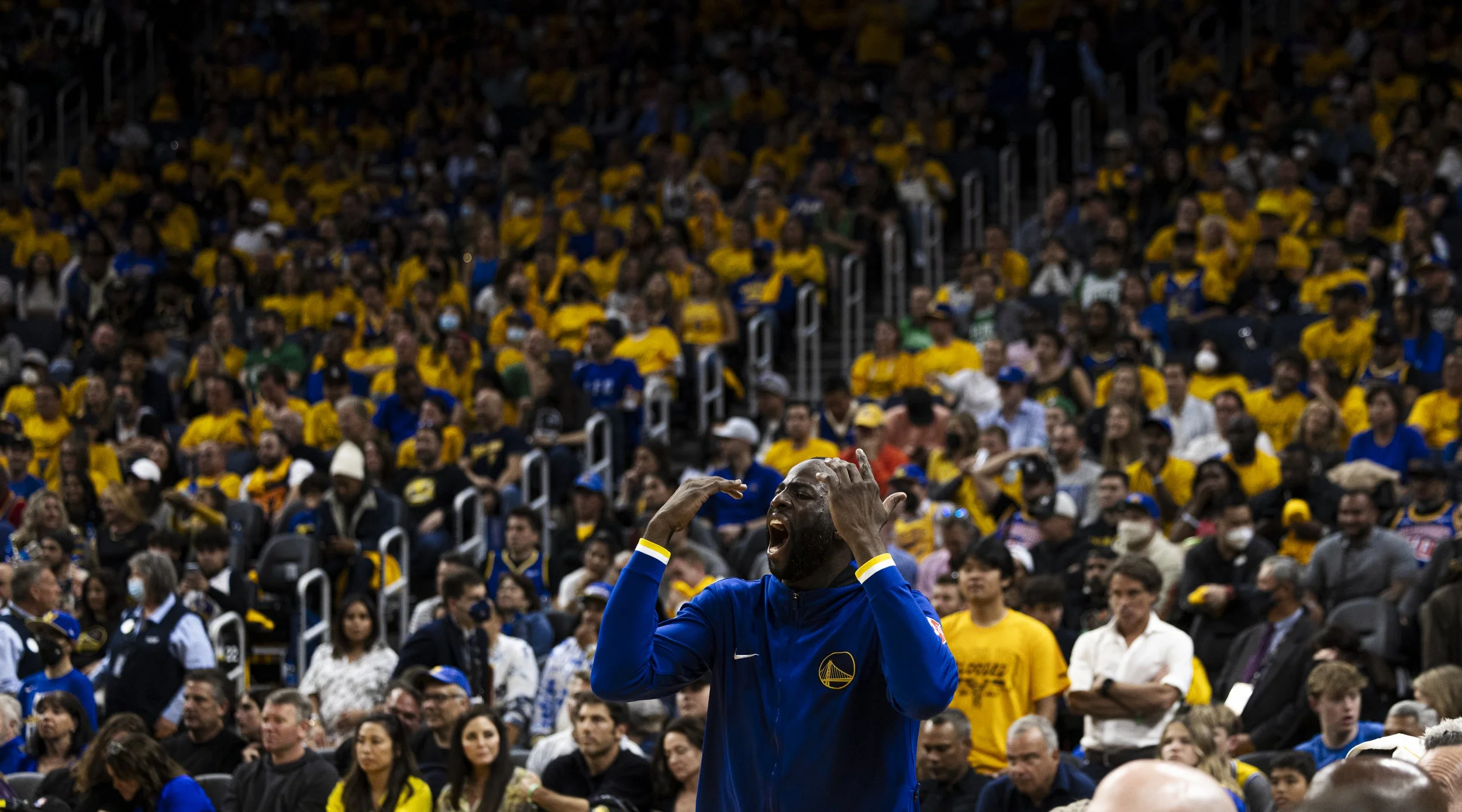 A basketball player in a blue jersey celebrating passionately in front of a large crowd wearing yellow at an indoor sports arena.