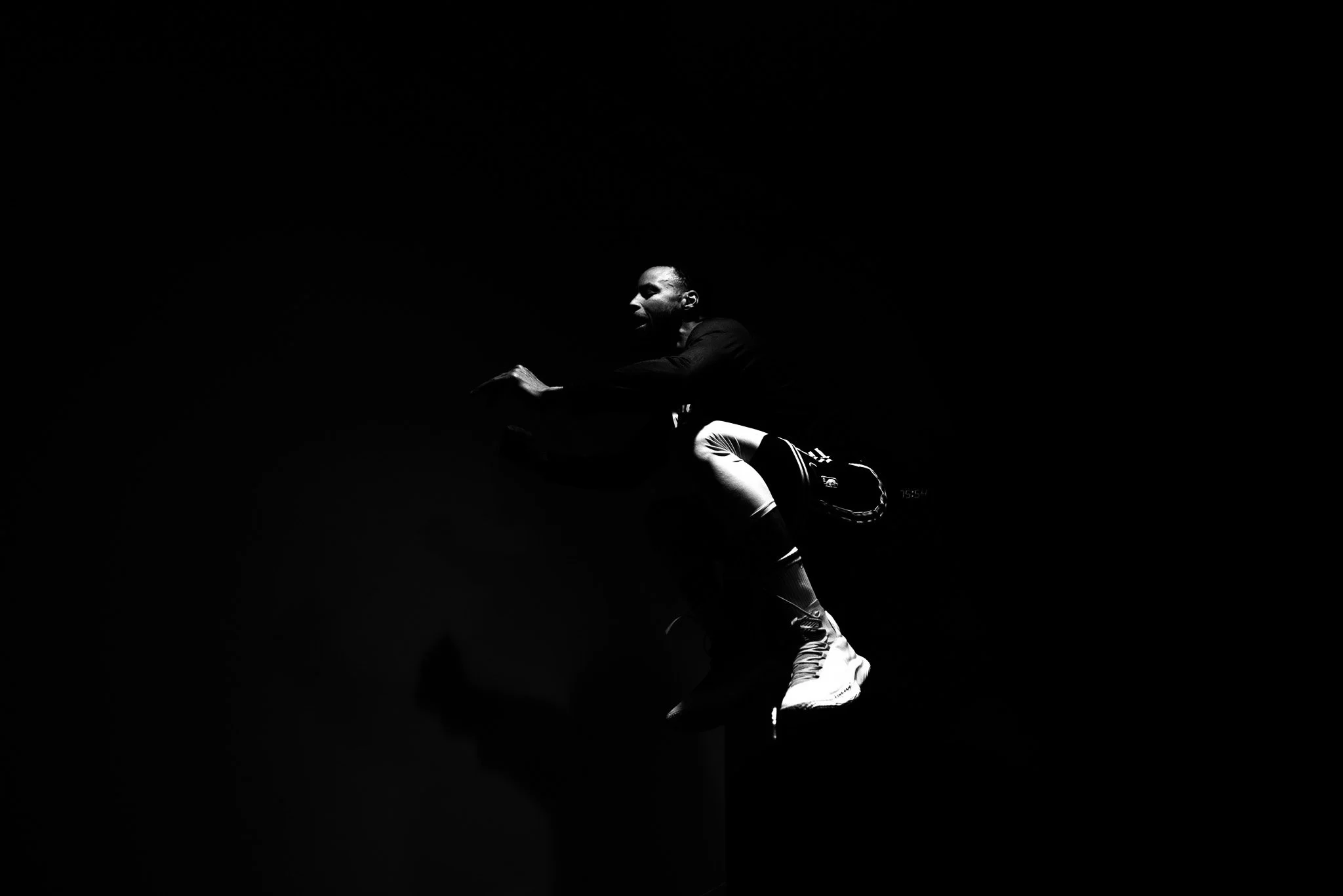 Black and white photograph of a person in athletic clothing, in a running pose, against a dark background.