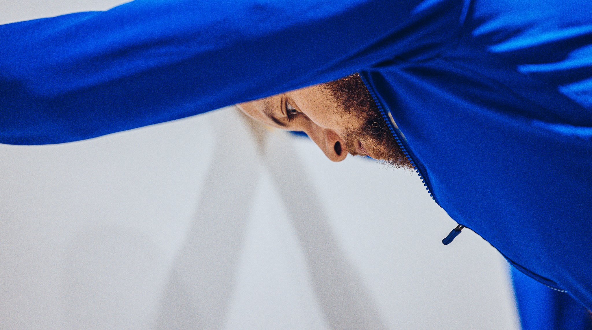 A person with curly hair wearing a blue jacket, looking downward, viewed from the side against a plain white background.