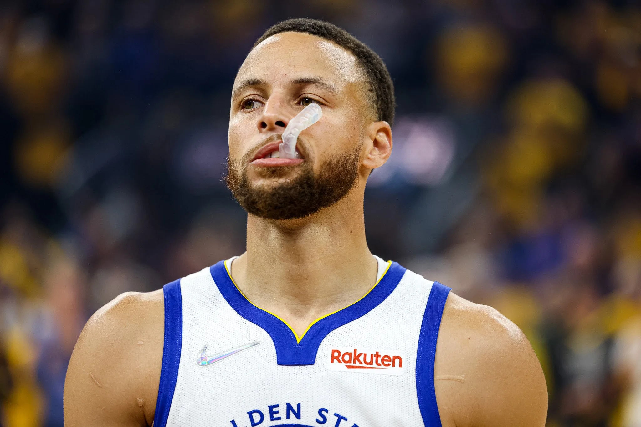 Basketball player with a beard and short hair wearing a white and blue jersey with Rakuten logo, standing on a basketball court.