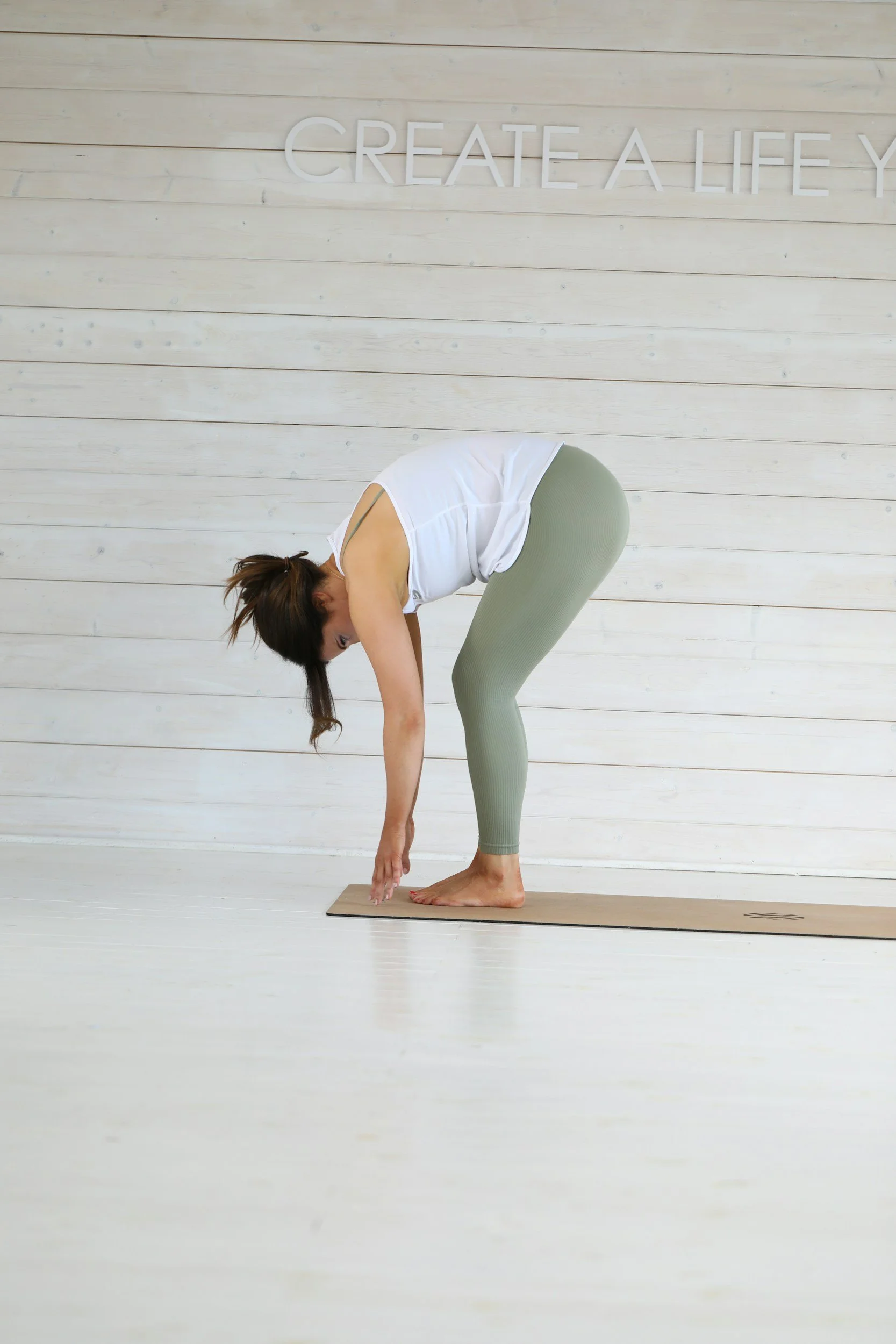Frau, die im Yoga-Posen steht, in einer hellen Yoga-Übungsraum mit weißen Holzwänden, reflektiert im Bild.