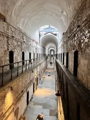 Interior view of a historic prison cell block with arched ceiling, stone floors, and cells on both sides, featuring metal bars and walkways.