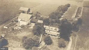 Aerial view of a rural farm with multiple buildings, trees, and surrounding fields.