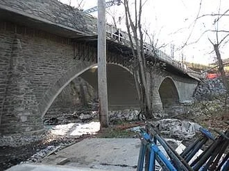 Stone bridge with three arches over a small stream, with leafless trees nearby and a bicycle in the foreground.