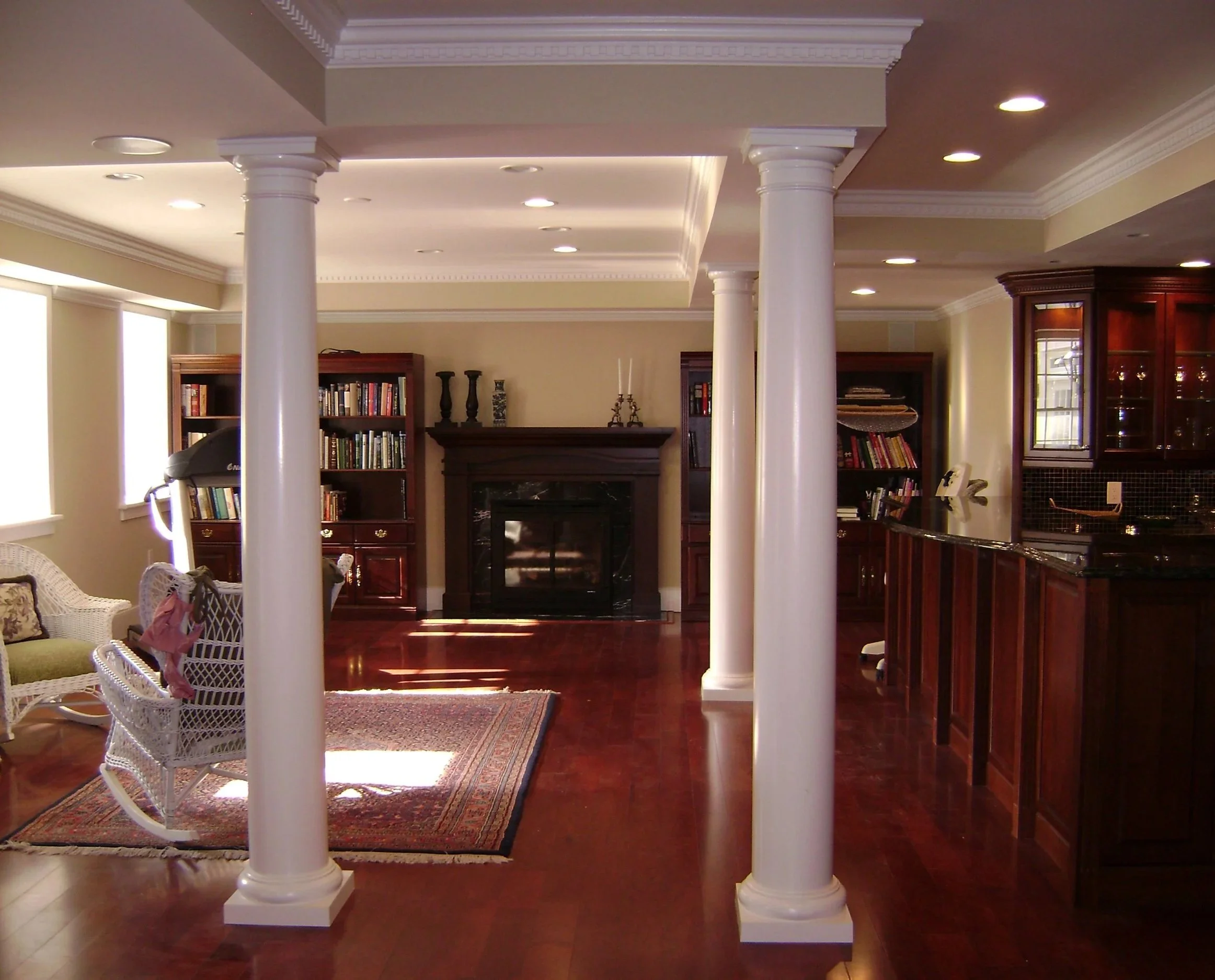 Interior view of a living room with white columns, bookshelves, a fireplace, and wooden furniture.