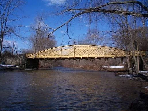 A wooden bridge over a river with leafless trees and a clear blue sky in the background.