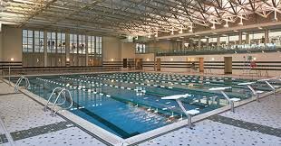 Indoor swimming pool with lane dividers and diving board, empty and well-lit.