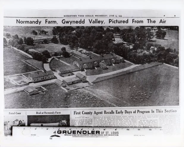 Aerial black and white photograph of Normandy Farm in Gwynned Valley. The farm includes multiple buildings, fields, and surrounding trees, with a ruler at the bottom for scale.