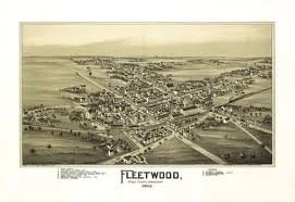 A historic aerial photograph of Fleetwood, showing a coastal town with buildings, streets, and a harbor, likely from the early 20th century.
