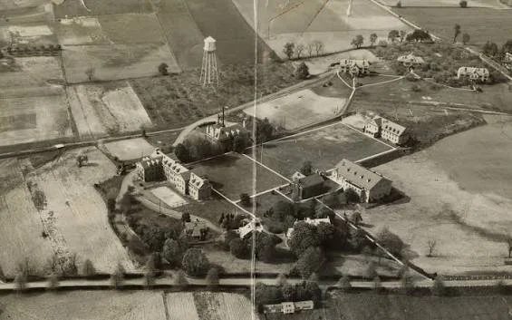 Aerial view of a farm with multiple buildings, a water tower, and fields surrounding the area.