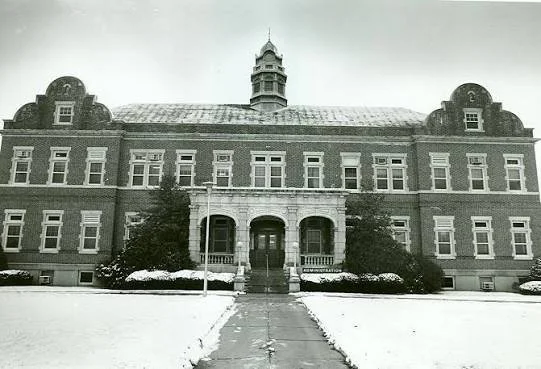 Historical brick building with a central tower, front steps, and surrounding snow-covered lawn.