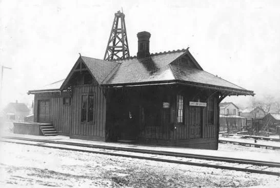 Old black and white photograph of a wooden train station with tracks in front, labeled as 'Mt. Lincoln,' and a mining derrick in the background.