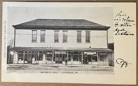 A black-and-white photo of a two-story building with shops on the ground floor and residential or office space above, labeled 'Watkins Male. Mooncie, PA.'