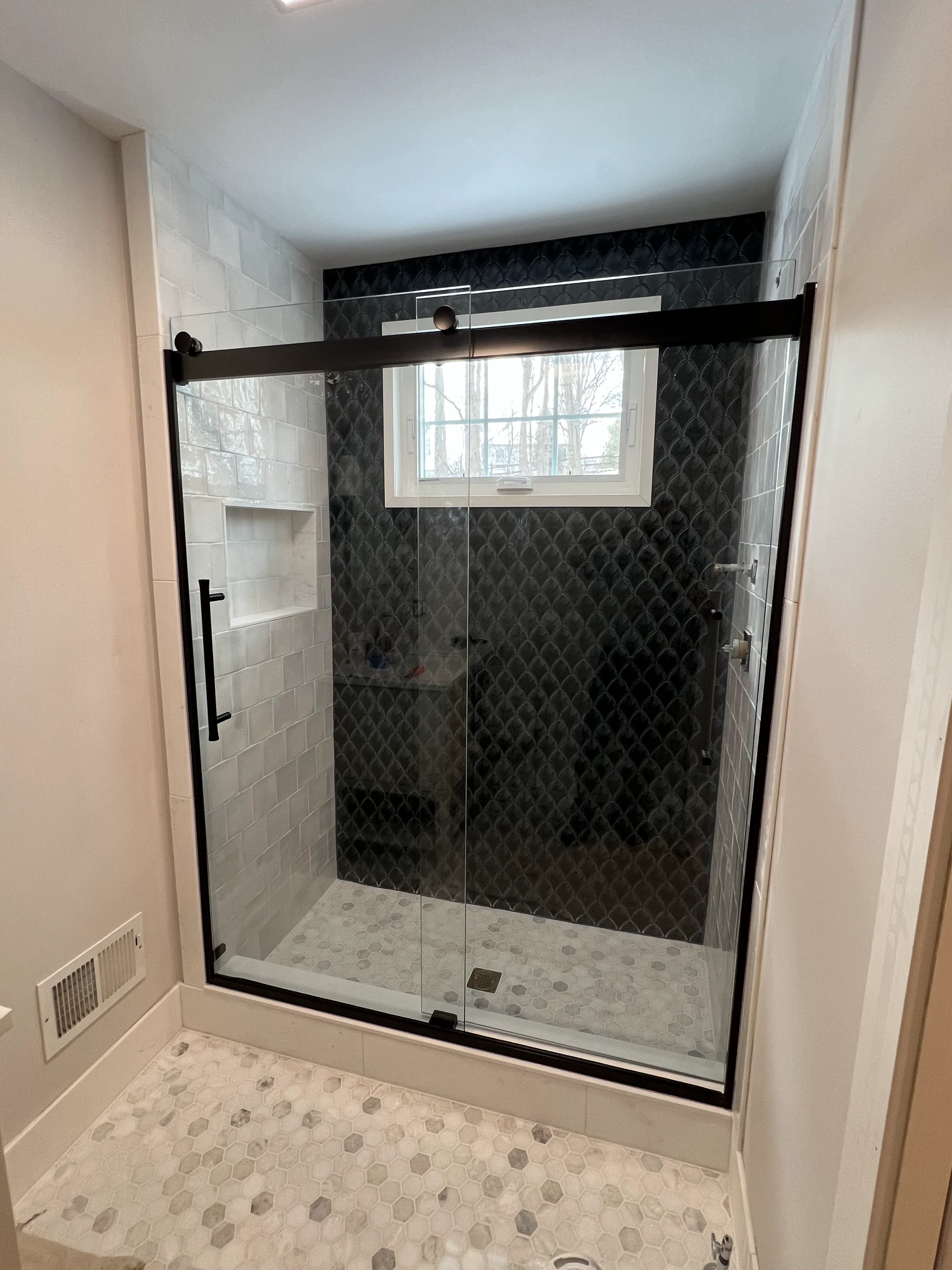 A modern glass shower stall with black and white tile design, a window, and a built-in shelf.
