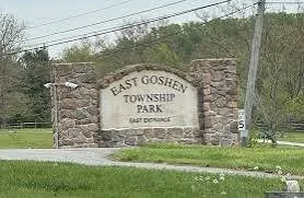 Sign reading East Goshen Township Park with stone pillars on either side, in a grassy area with trees and power lines in the background.