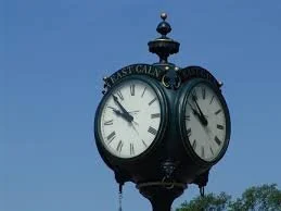 A vintage street clock with two faces showing the time, mounted on a pole against a blue sky.