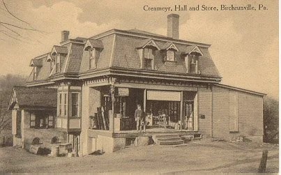 Sepia image of the Cremery, Hall, and Store in Birchrunville, Pennsylvania, showing a two-story wooden building with a large storefront, porch, and people standing outside.
